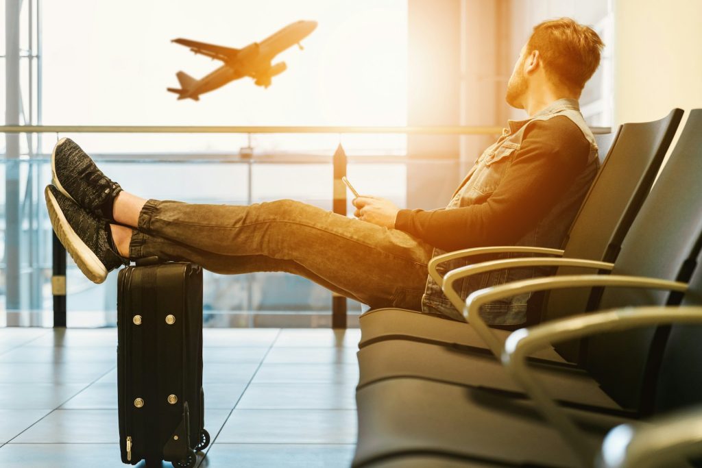 Traveller with a carry-on suitcase watching a plane take off from an airport departure lounge