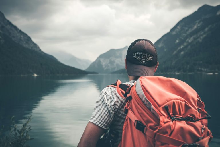 Solo traveller with a backpack looking out over a mountain lake